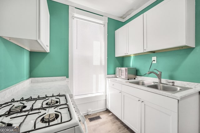 kitchen featuring white range with gas cooktop, white cabinets, light countertops, and a sink