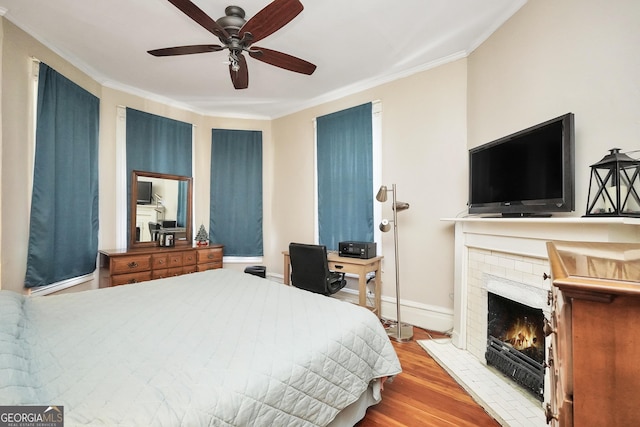 bedroom featuring wood finished floors, baseboards, ceiling fan, crown molding, and a brick fireplace