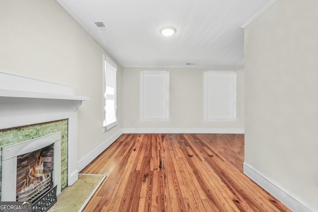 unfurnished living room with visible vents, a lit fireplace, crown molding, light wood finished floors, and baseboards