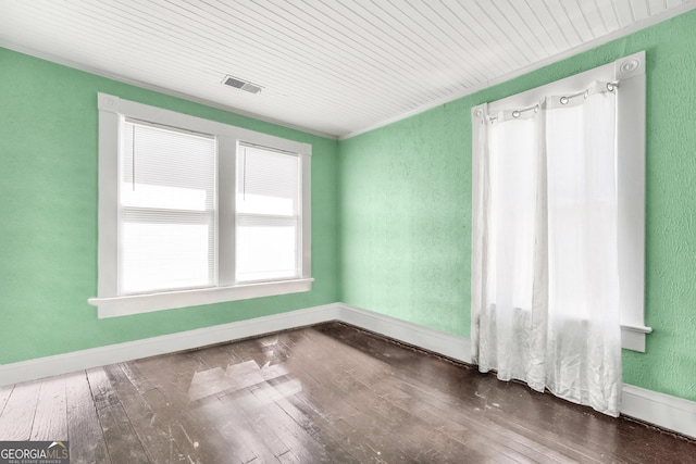 spare room featuring visible vents, baseboards, dark wood-style flooring, and a textured wall