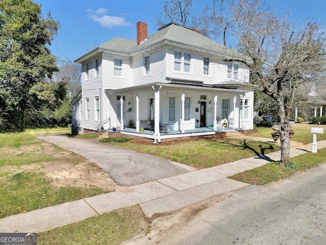 view of front of property featuring a porch, a chimney, a front yard, and roof with shingles