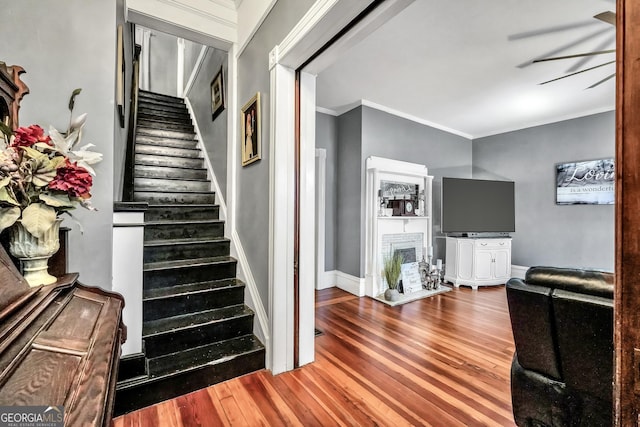 stairs featuring wood finished floors, a fireplace, baseboards, and ornamental molding