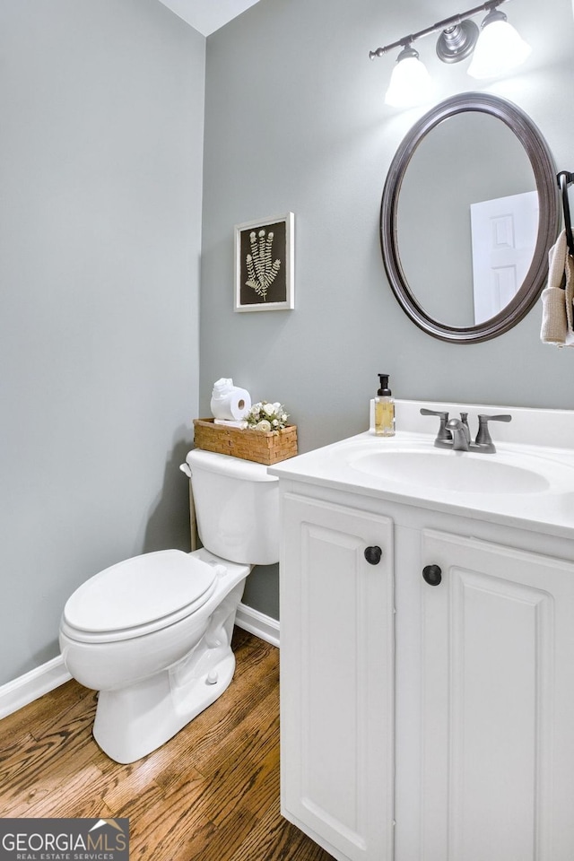 bathroom with toilet, vanity, baseboards, and wood finished floors