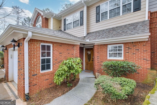 entrance to property with an attached garage, brick siding, and a shingled roof