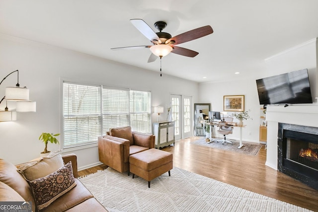 living room featuring baseboards, a ceiling fan, a lit fireplace, and wood finished floors