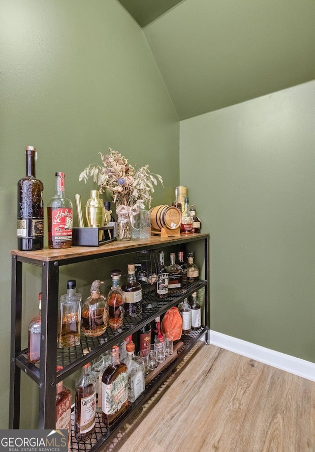 bar with baseboards, lofted ceiling, a bar, and wood finished floors