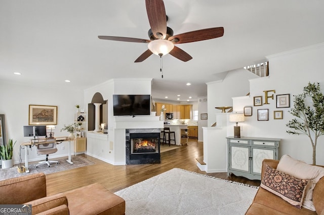 living area with recessed lighting, a premium fireplace, wood finished floors, and crown molding