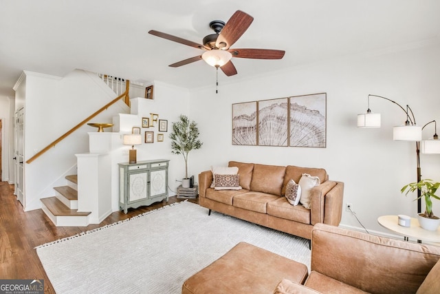 living area featuring wood finished floors, a ceiling fan, ornamental molding, and stairs