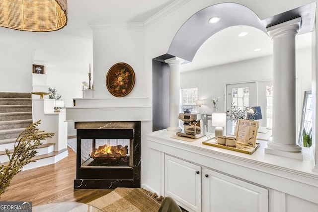 bar with a multi sided fireplace, stairway, light wood-type flooring, ornamental molding, and ornate columns