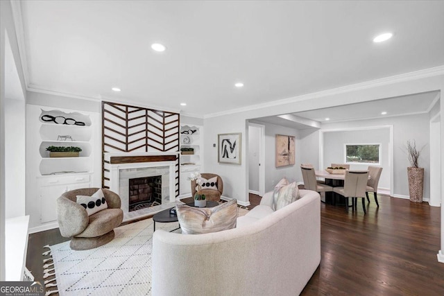 living area featuring a fireplace with raised hearth, built in shelves, crown molding, and wood finished floors