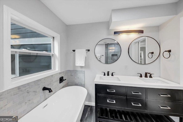 full bathroom with double vanity, a freestanding tub, wood finished floors, and a sink