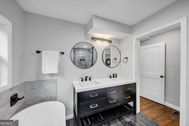 full bath with a sink, a freestanding bath, wood finished floors, and double vanity