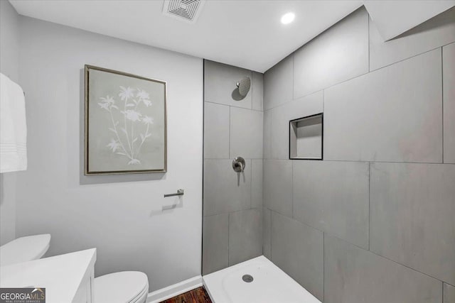 bathroom featuring visible vents, toilet, baseboards, tiled shower, and vanity