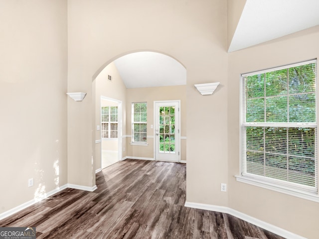 unfurnished room with visible vents, dark wood-style floors, baseboards, arched walkways, and lofted ceiling