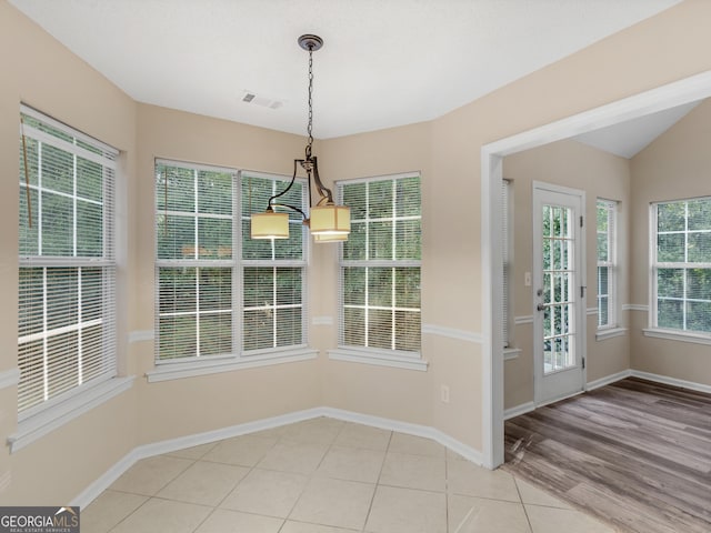 unfurnished dining area featuring visible vents, baseboards, lofted ceiling, an inviting chandelier, and tile patterned floors