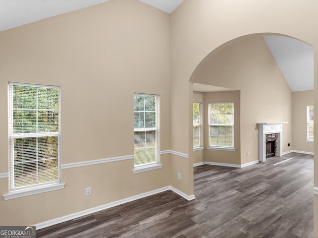 unfurnished living room featuring dark wood finished floors, arched walkways, high vaulted ceiling, and a high end fireplace