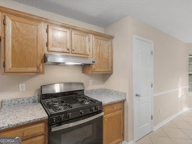 kitchen with black gas stove, light stone countertops, under cabinet range hood, light tile patterned floors, and a textured ceiling