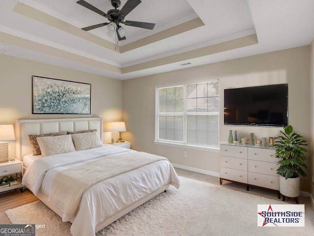 bedroom featuring visible vents, ceiling fan, baseboards, a tray ceiling, and ornamental molding