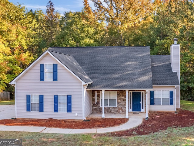 traditional-style home with stone siding, a porch, a chimney, and a shingled roof