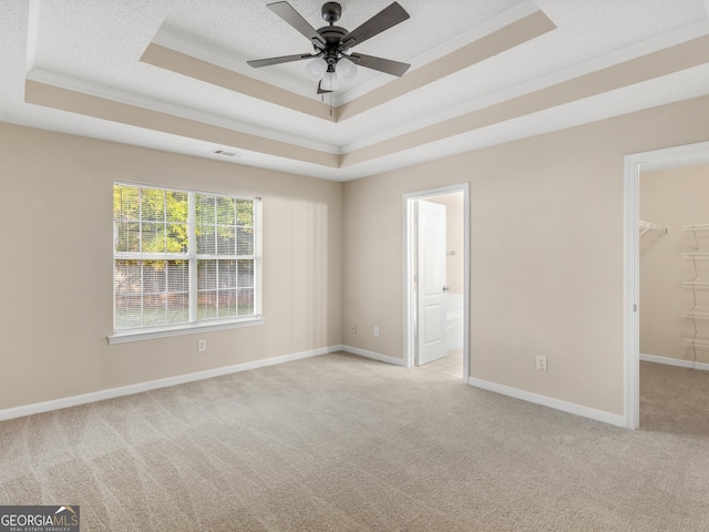 unfurnished room with light carpet, a tray ceiling, a textured ceiling, crown molding, and baseboards