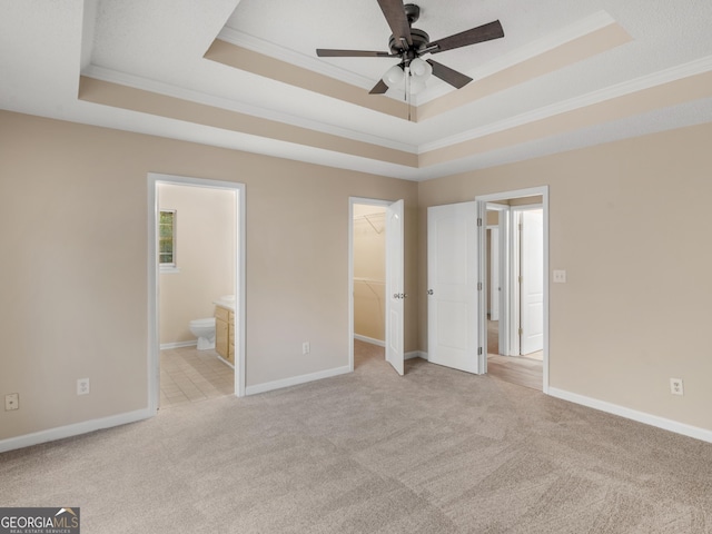 unfurnished bedroom featuring light carpet, a spacious closet, crown molding, and a tray ceiling