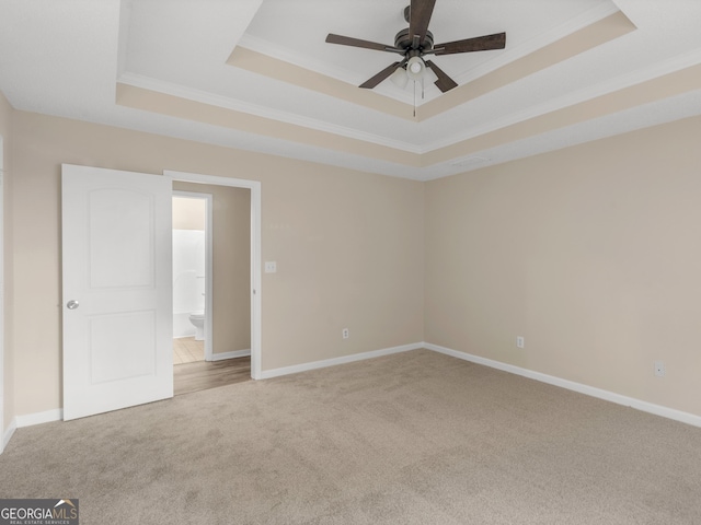 carpeted spare room featuring crown molding, baseboards, a raised ceiling, and a ceiling fan