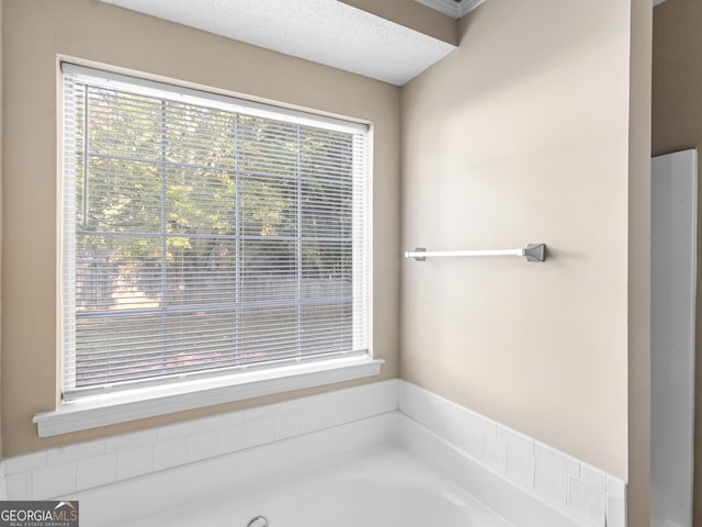 full bath with a wealth of natural light, a textured ceiling, and a garden tub