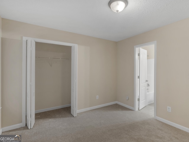 unfurnished bedroom featuring baseboards, ensuite bath, carpet floors, a closet, and a textured ceiling