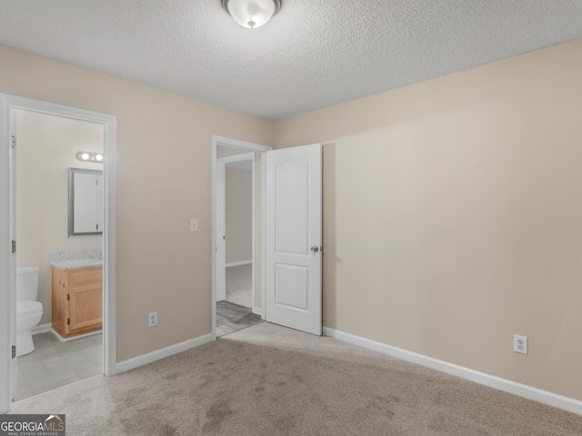 unfurnished bedroom featuring a textured ceiling, baseboards, ensuite bathroom, and light carpet