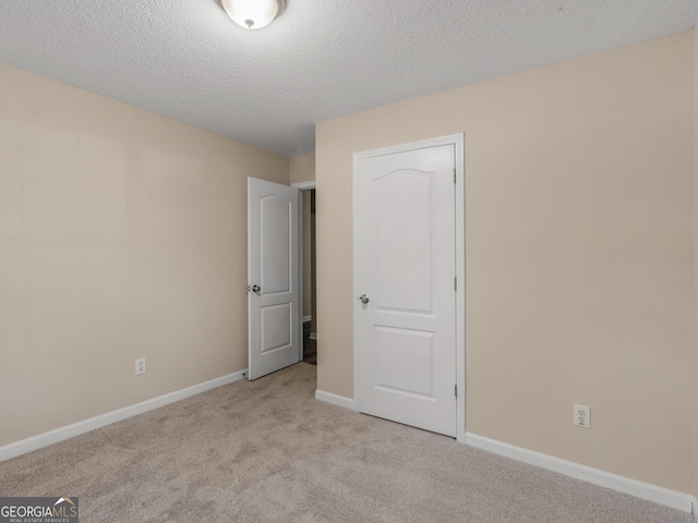 unfurnished bedroom featuring light carpet, a textured ceiling, and baseboards