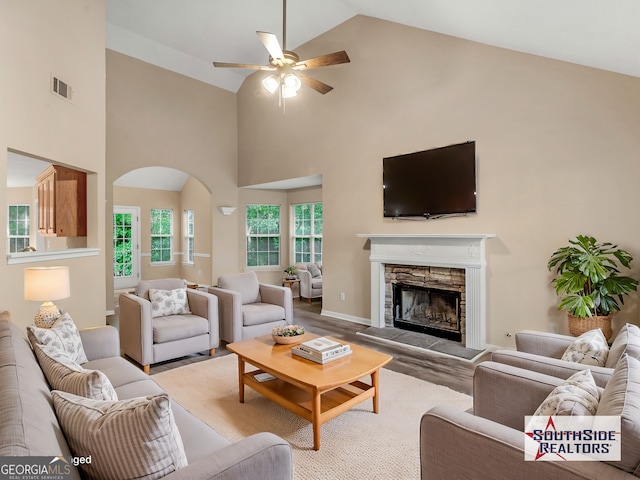 living area featuring visible vents, ceiling fan, a fireplace, wood finished floors, and arched walkways