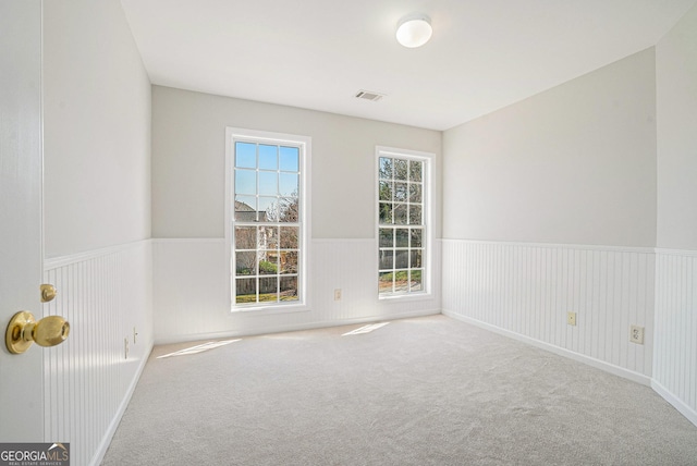 carpeted empty room featuring visible vents and wainscoting