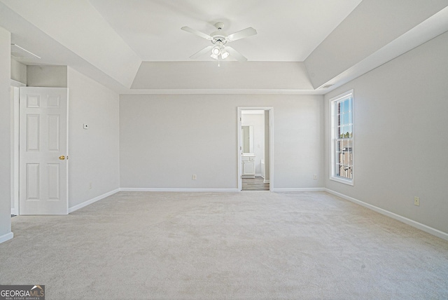 spare room featuring light colored carpet, baseboards, a tray ceiling, and a ceiling fan