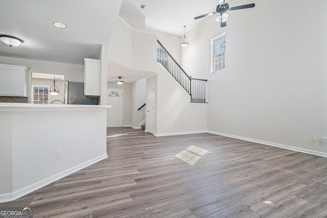 unfurnished living room featuring stairway, a ceiling fan, baseboards, and wood finished floors