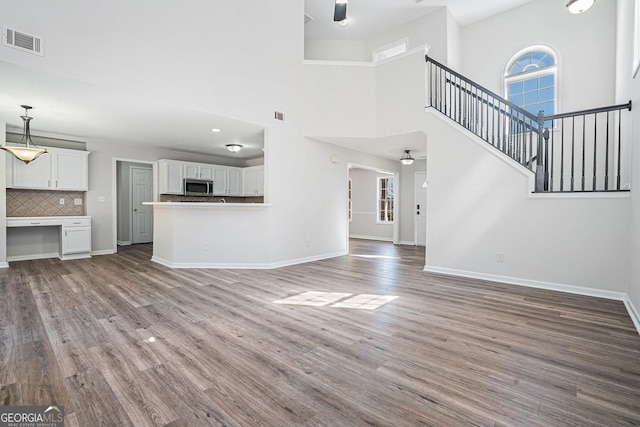 unfurnished living room featuring visible vents, baseboards, wood finished floors, and stairs