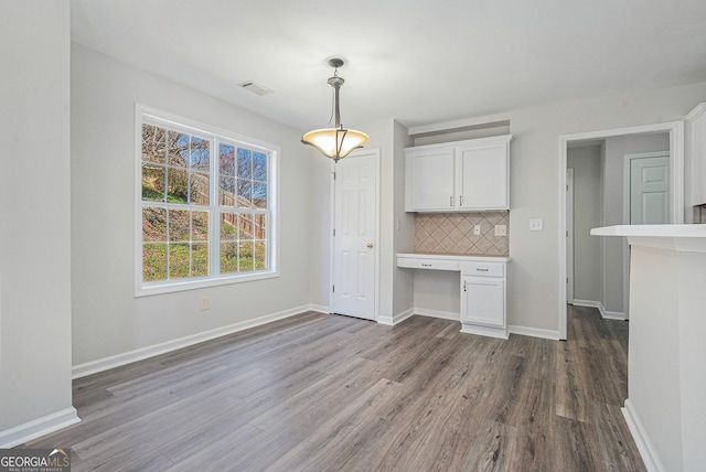 unfurnished dining area with baseboards, wood finished floors, and built in desk