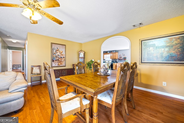 dining area featuring visible vents, light wood-style flooring, a textured ceiling, arched walkways, and baseboards