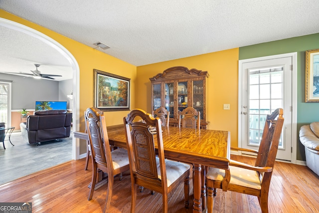 dining room with a wealth of natural light, visible vents, arched walkways, and light wood finished floors