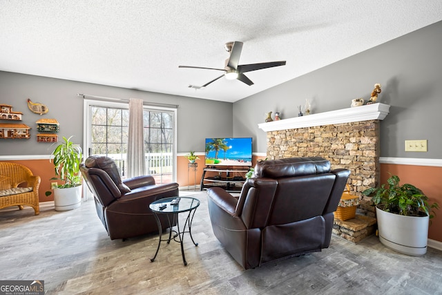 living room featuring a ceiling fan, wood finished floors, wainscoting, and a textured ceiling