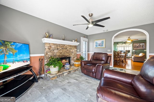 living area with ceiling fan, arched walkways, wood finished floors, and a fireplace