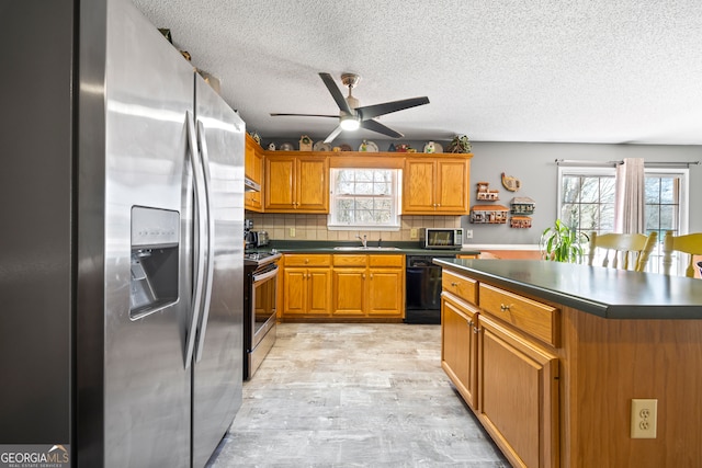 kitchen with a sink, stainless steel appliances, dark countertops, and brown cabinetry