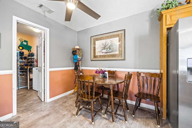 dining room featuring visible vents, a textured ceiling, wood finished floors, baseboards, and ceiling fan