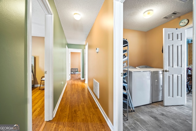 hallway featuring visible vents, washing machine and dryer, a textured ceiling, and wood finished floors