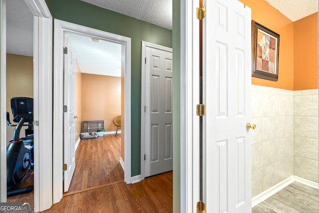 hallway with baseboards, a textured ceiling, and wood finished floors