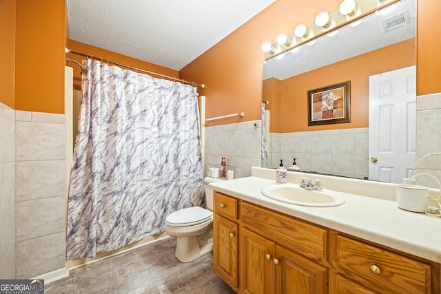 full bathroom featuring visible vents, toilet, a textured ceiling, tile walls, and vanity