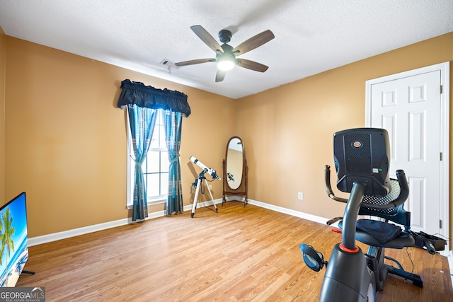 workout area featuring ceiling fan, light wood-style flooring, baseboards, and a textured ceiling