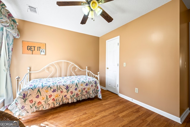 bedroom with a ceiling fan, wood finished floors, visible vents, baseboards, and a textured ceiling