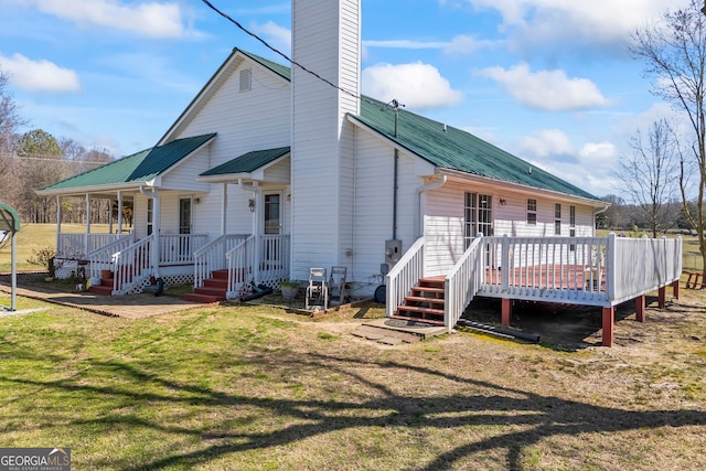 rear view of house featuring a porch, a lawn, a chimney, and metal roof