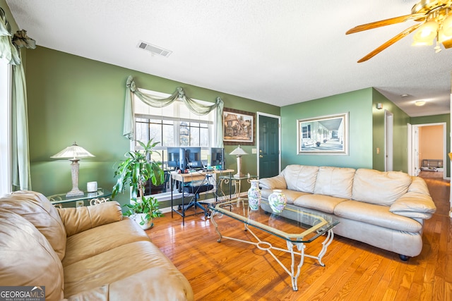 living room featuring ceiling fan, visible vents, a textured ceiling, and wood finished floors