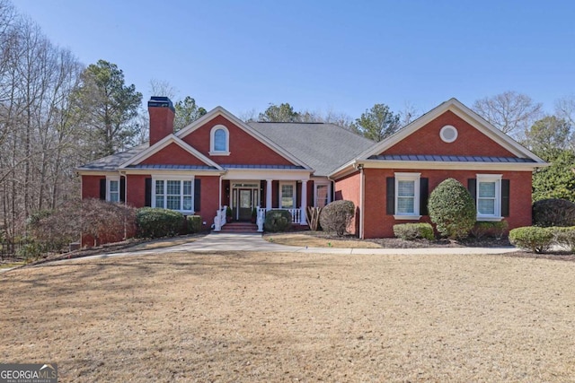 view of front of home featuring brick siding, covered porch, a chimney, and a standing seam roof